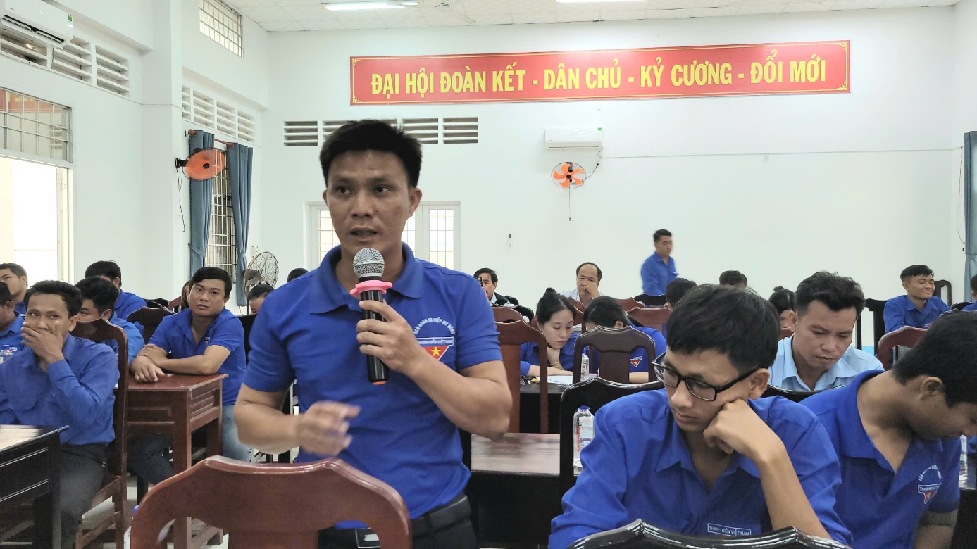 A person in blue shirt speaking into a microphone

Description automatically generated