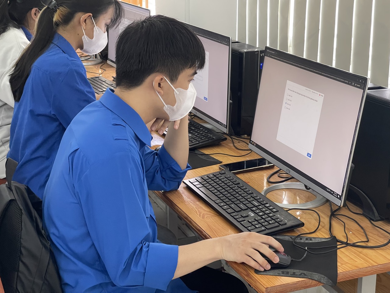 A person wearing a mask and sitting at a desk with a computer

Description automatically generated